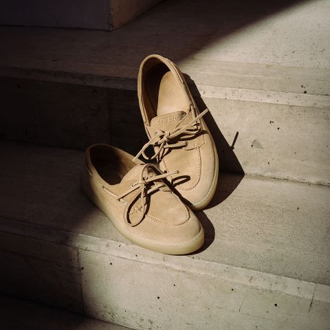 Un par de zapatos náuticos de ante beige con cordones, que descansan sobre escalones de hormigón soleados.