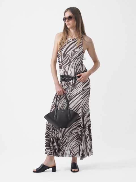 Mujer con gafas de sol, vistiendo un vestido maxi estampado en blanco y negro, un cinturón negro y sandalias negras, y sosteniendo un bolso de mano negro frente a un fondo blanco.