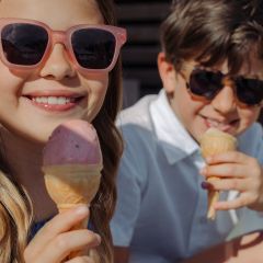 Dos niños sonrientes con gafas de sol disfrutan de conos de helado al aire libre en un día soleado.