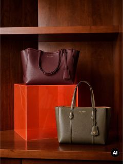 Dos bolsos de cuero, uno en color burdeos y otro en verde oliva, presentados en estantes de madera junto con un bloque acrílico naranja.