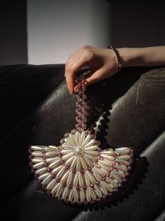 Una mano sostiene un bolso de mano con cuentas con diseños de perlas y flores rosas, que descansa sobre una superficie de cuero negro texturizado.