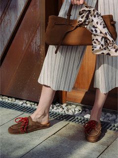 Persona que lleva unos pantalones de pernera ancha a rayas y mocasines marrones con cordones rojos, y sostiene un bolso de mano marrón con un pañuelo de estampado de leopardo anudado al asa.