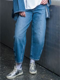Una persona que lleva vaqueros azules, una chaqueta vaquera, calcetines blancos y zapatillas de deporte grises está de pie en una casa junto a una superficie metálica.